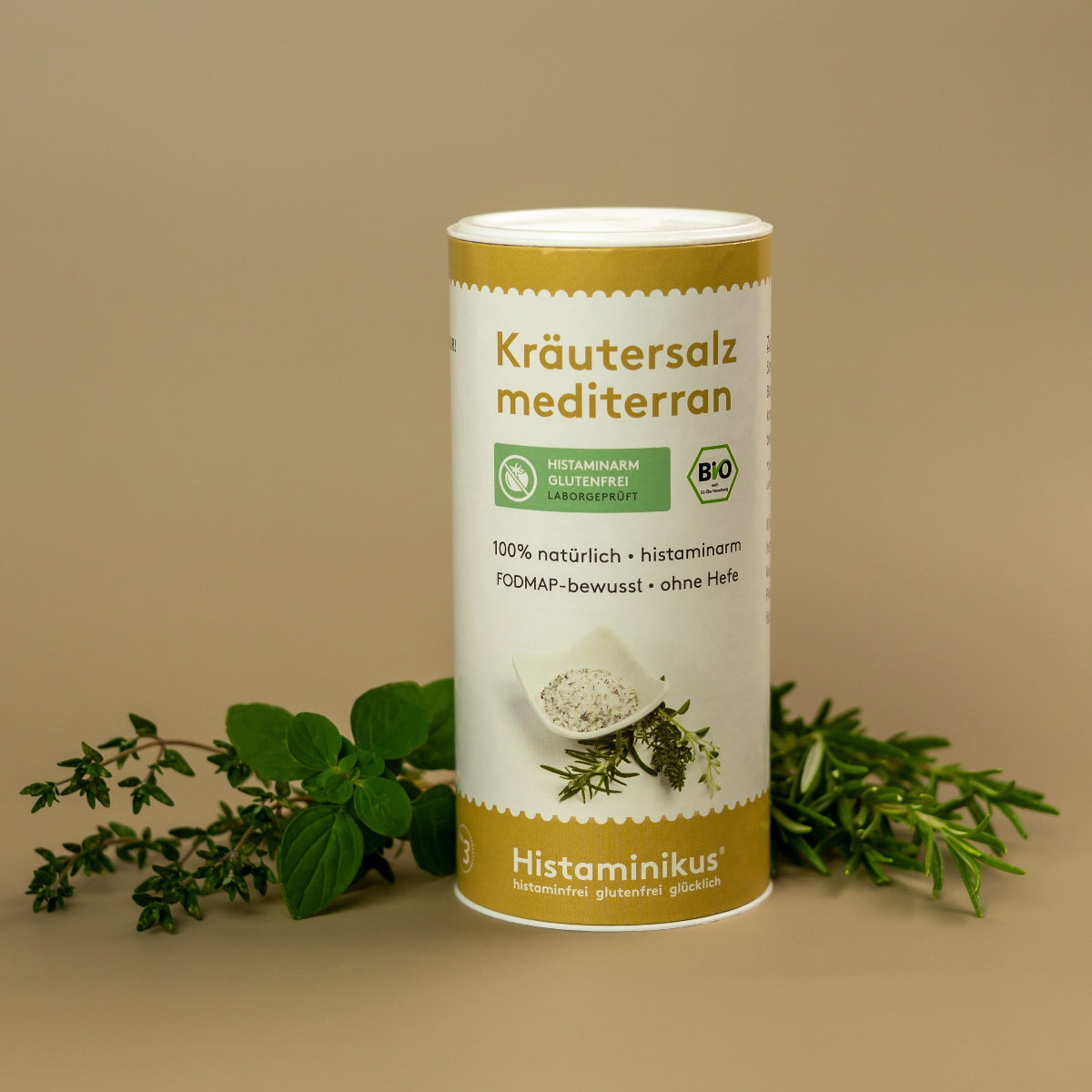 Weiße Gewürzdose mit goldgelbem Rand und der Aufschrift „Kräutersalz mediterran“. Darunter grüne Siegel „Histaminarm glutenfrei – laborgeprüft“ und „Bio“. In der Mitte ein Schälchen mit Kräutersalz und frischen Kräutern. Im Hintergrund frische Kräuterzweige auf beigem Untergrund. Unten goldener Bereich mit dem Logo von Histaminikus.