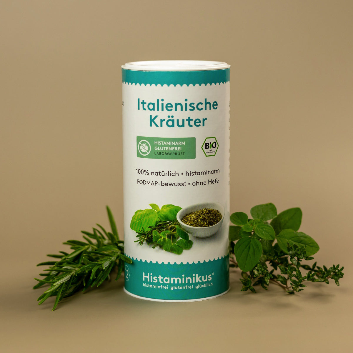 Weiße Gewürzdose mit Aufschrift „Italienische Kräuter“ und Labeln „histaminarm, glutenfrei, laborgeprüft“ sowie Bio-Siegel. Davor frische Kräuter wie Rosmarin, Oregano und Thymian, daneben eine kleine Schale mit getrockneten Kräutern.