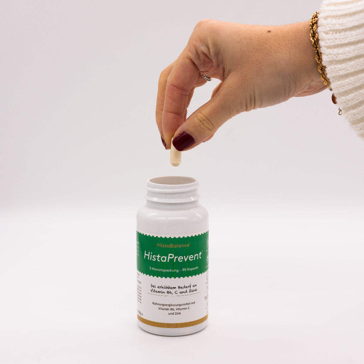 Eine Hand mit dunkel lackierten Fingern hält eine Kapsel über eine offene Dose „HistaPrevent“ von HistaBalance®