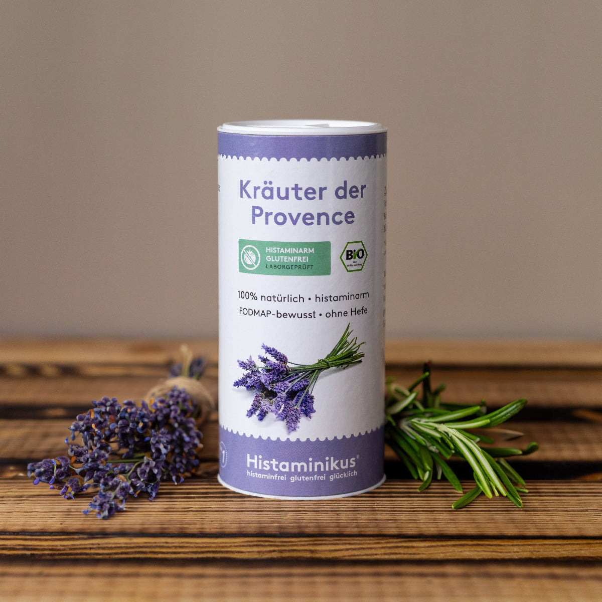 Produktaufnahme einer Gewürzdose mit der Aufschrift „Kräuter der Provence“. Die Dose steht auf einem Holzuntergrund und ist von frischem Lavendel und Rosmarin umgeben. Auf dem Etikett sind neben dem Produktnamen auch Hinweise wie „histaminarm“, „glutenfrei“, „FODMAP-bewusst“ und „ohne Hefe“ sowie ein Lavendelmotiv zu sehen. Das Design ist in Weiß und Violett gehalten mit dem grünen Bio-Siegel und dem Histaminikus-Logo.