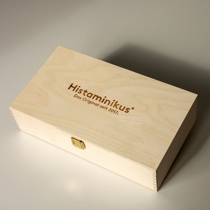 Geschlossene Holzbox mit Messingverschluss auf hellem Untergrund. Auf dem Deckel ist der Schriftzug „Histaminikus“ eingraviert.