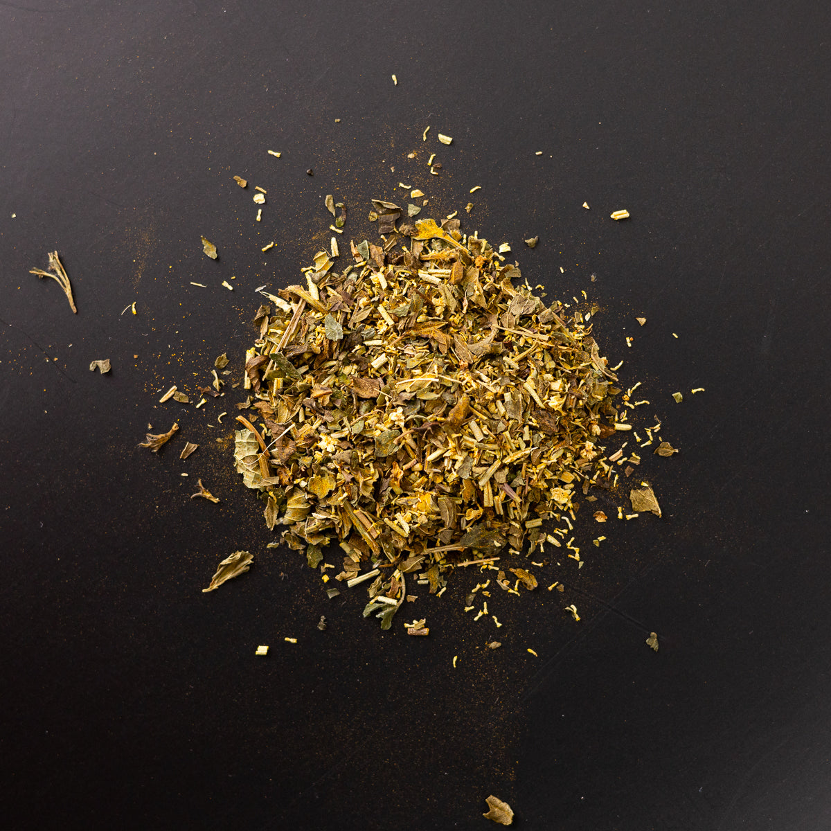 Loser Kräutertee in goldgrüner Farbgebung auf schwarzem Untergrund, Mischung mit erkennbaren Blatt-, Blüten- und Stängelanteilen, darunter feinere gelbliche und bräunliche Bestandteile.