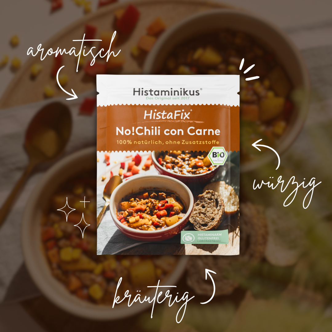 Zentral platzierter HistaFix-Beutel „No!Chili con Carne“ von Histaminikus auf einem leicht unscharfen Hintergrund mit dampfendem Chili-Gericht, umgeben von handschriftlichen Beschreibungen wie „aromatisch“, „würzig“ und „kräuterig“, mit Bio-Siegel und grünem Hinweis „histaminarm, glutenfrei, laborgeprüft“.