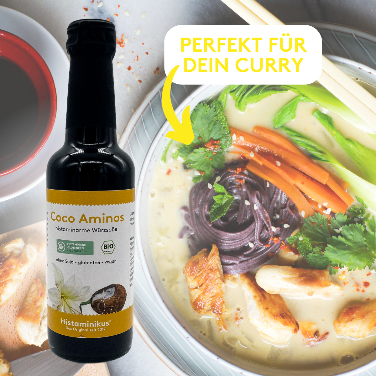 Werbegrafik mit Flasche „Coco Aminos – histaminarme Würzsoße“ links im Bild. Rechts eine Curry-Bowl mit Gemüse, Hähnchen und violetten Nudeln. Gelber Pfeil zeigt auf das Gericht, daneben Text: „Perfekt für dein Curry“.