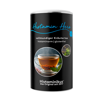 Schwarze Teedose mit der Aufschrift „Histamin Hero – vollmundiger Kräutertee“, darunter „histaminarm | glutenfrei“. In der Mitte ein rundes Foto mit dampfender Tasse Kräutertee auf einem Holzuntergrund, daneben zwei kleine Pflanzenabbildungen.