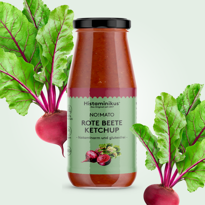 Abbildung der Flasche des Rote Beete Ketchup in der Mitte des Bildes. Links und rechts neben der Flasche sind rote Beete Rüben mit Blättern zu sehen.