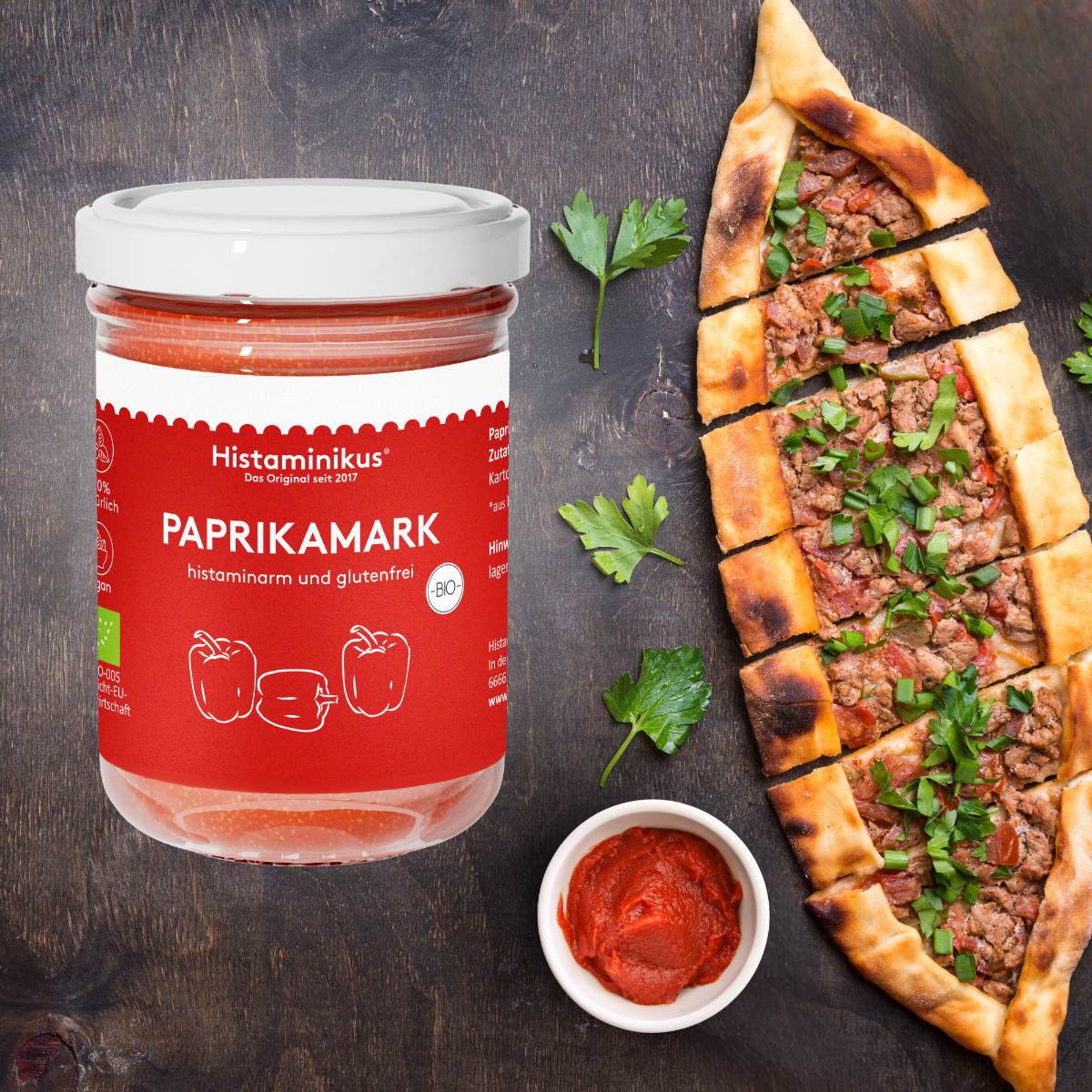 Grafik mit dem Paprikamark-Glas auf der linken Seite. Daneben ist ein Pide zu sehen vor dem ein kleines Schälchen mit dem Paprikamark steht. Der Hintergrund ist aus dunklem Holz.
