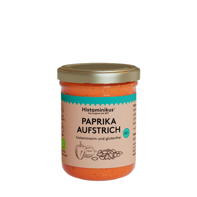 Glas mit orangem Inhalt und goldenem Deckel. Etikett mit der Aufschrift: Paprikaaufstrich. Der Inhalt wird als histaminarm und glutenfrei bezeichnet. Außerdem sind auf dem Etikett zwei Paprika und Kürbiskerne zu sehen. Das Bio-Siegel ist rechts in einem kräftigen Türkis aufgedruckt.