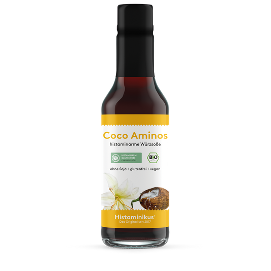 Große Glasflasche (245 ml) mit schwarzem Deckel und Etikett „Coco Aminos – histaminarme Würzsoße“. Abbildung einer Kokosnuss und Blüte, mit Bio- und histaminarm-Siegel. Aufschrift: ohne Soja, glutenfrei, vegan.