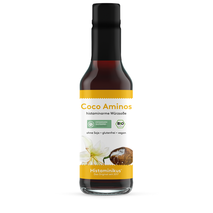 Große Glasflasche (245 ml) mit schwarzem Deckel und Etikett „Coco Aminos – histaminarme Würzsoße“. Abbildung einer Kokosnuss und Blüte, mit Bio- und histaminarm-Siegel. Aufschrift: ohne Soja, glutenfrei, vegan.