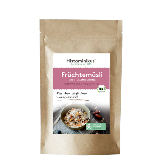 Braune Papierverpackung mit weißem Etikett. Produktname „Früchtemüsli“ in rosa Schrift, darunter „Bio-Müslimischung, histaminarm und glutenfrei“. Foto einer Müslischale mit Löffel und Trockenfrüchten.