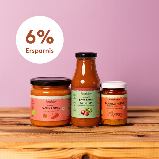 Drei histaminarme Produkte von Histaminikus – NO!MATO Paprikasoße, Rote-Bete-Ketchup und Paprika-Pesto – nebeneinander auf einem Holztisch vor violettem Hintergrund.