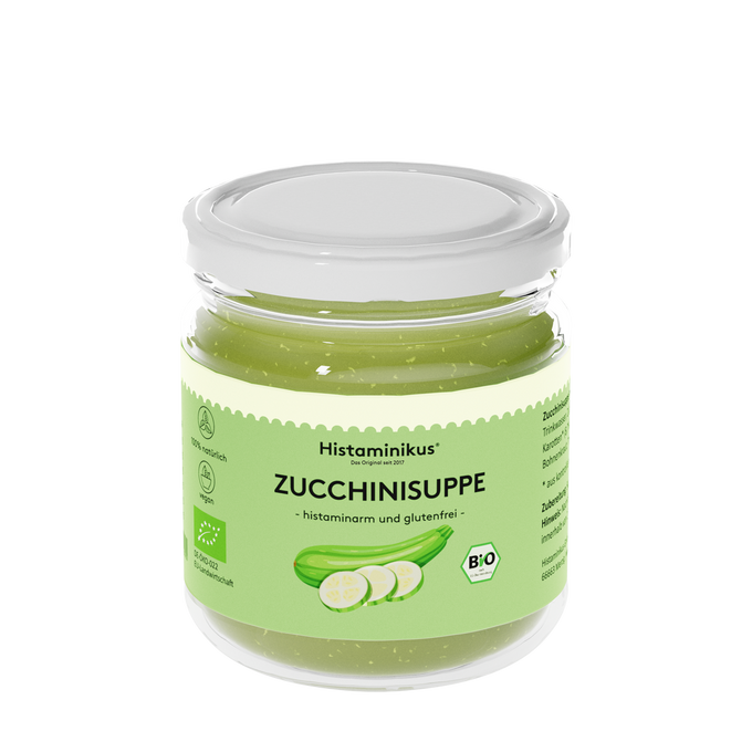 Ein Glas mit weißem Deckel, gefüllt mit hellgrüner Zucchinisuppe. Auf dem Etikett steht „Histaminikus – Das Original seit 2017“, darunter in Schwarz „ZUCCHINISUPPE – histaminarm und glutenfrei“. Abgebildet ist eine grüne Zucchini mit drei Zucchinischeiben. Symbole weisen auf 100 % natürliche Zutaten, Veganität und EU-Bio-Zertifizierung hin.