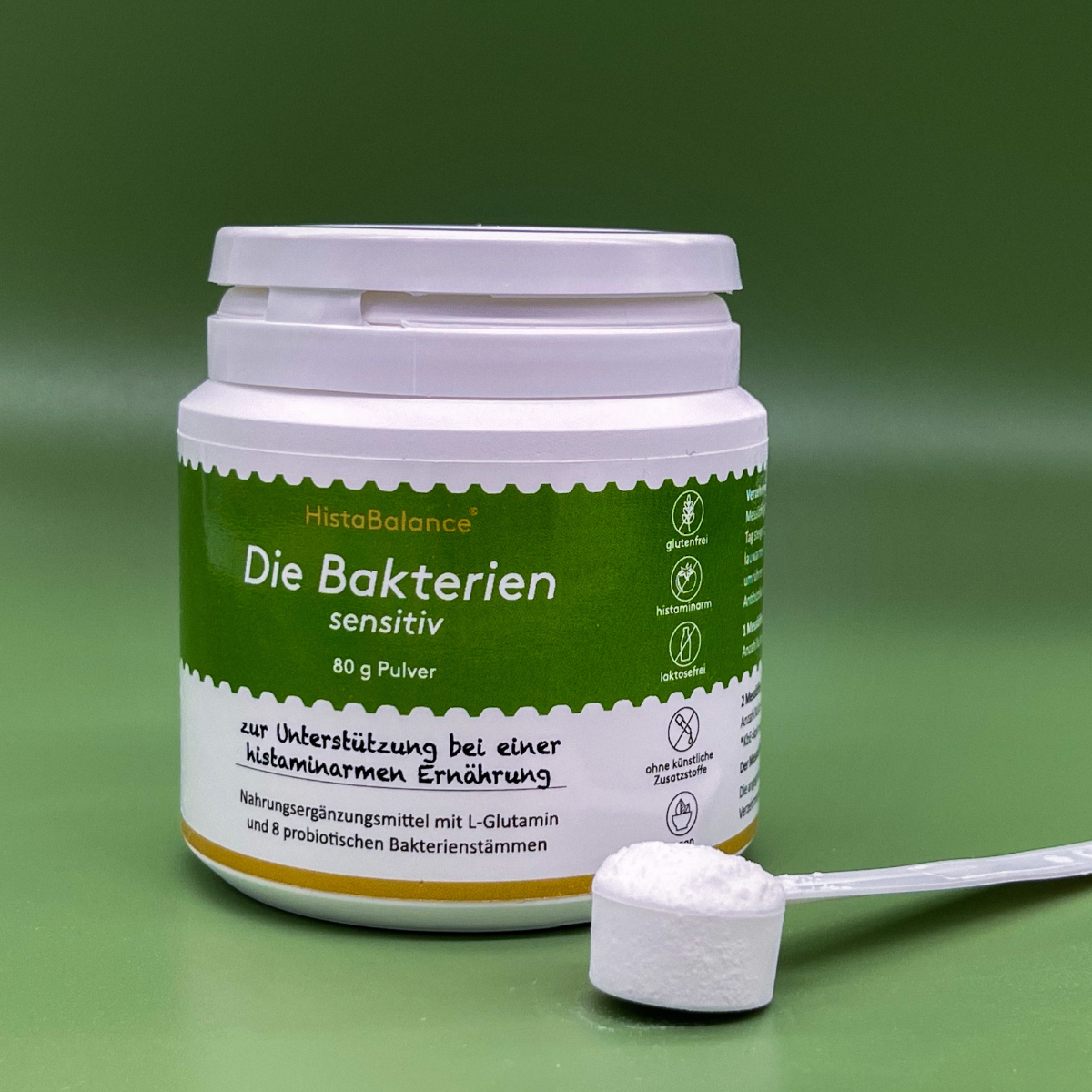Geöffnete Dose „Die Bakterien sensitiv“ von HistaBalance auf grünem Hintergrund. Das Etikett zeigt Hinweise auf Histaminarmut, Glutenfreiheit, Laktosefreiheit und Verzicht auf Zusatzstoffe. Im Vordergrund liegt ein gefüllter Messlöffel mit dem weißen Pulver.