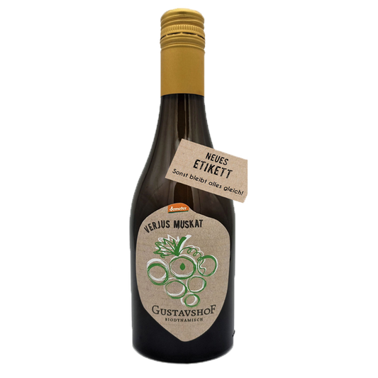 Braune Glasflasche mit goldfarbenem Schraubverschluss. Auf dem Etikett steht „VERJUS MUSKAT“ sowie „Gustavshof – Biodynamisch“ mit einer stilisierten grünen Traubengrafik. Ein zusätzlicher Anhänger am Flaschenhals trägt die Aufschrift „NEUES ETIKETT – Sonst bleibt alles gleich!“.