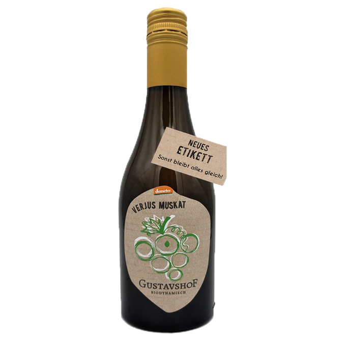 Braune Glasflasche mit goldfarbenem Schraubverschluss. Auf dem Etikett steht „VERJUS MUSKAT“ sowie „Gustavshof – Biodynamisch“ mit einer stilisierten grünen Traubengrafik. Ein zusätzlicher Anhänger am Flaschenhals trägt die Aufschrift „NEUES ETIKETT – Sonst bleibt alles gleich!“.