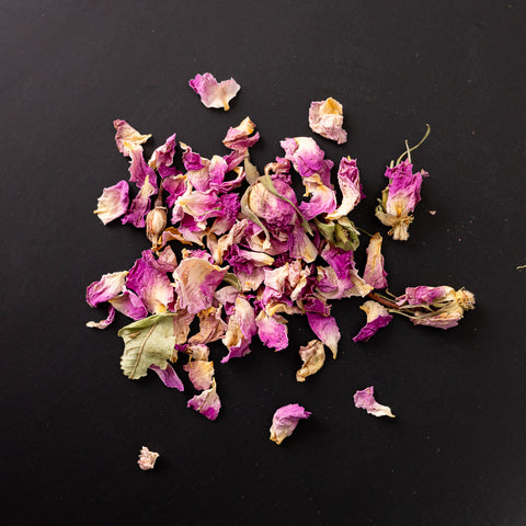 Eine Handvoll getrockneter rosa Rosenblütenblätter locker auf schwarzem Untergrund verteilt.