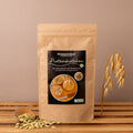 Braune Papiertüte mit schwarzem Produktetikett „Histaminikus Proteinbrötchen“ mit Foto von den Brötchen, neben der Tüte ein Holzlöffel mit Kürbiskernen und Haferhalm-Deko auf Holzuntergrund.
