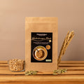 Stehende Papierverpackung „Winterknusper Müsli“ von Histaminikus auf einer Holzoberfläche, davor eine Glasschale mit Haferflocken und verstreute Kürbiskerne, rechts daneben Getreideähren, warmes beigefarbenes Hintergrundlicht.