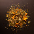 Teemischung aus Rooibos mit getrockneten Mangostücken und Kräutern, lose auf dunklem Hintergrund ausgebreitet.