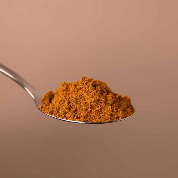 Fein gemahlenes asiatisches Gewürzpulver auf einem Löffel vor schlichtem Hintergrund.