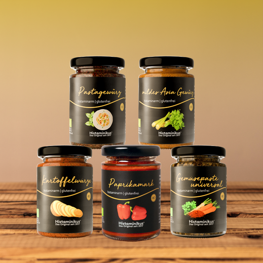 Fünf histaminarme, glutenfreie Produkte von Histaminikus in Gläsern: Pastagewürz, mildes Asia Gewürz, Kartoffelwürze, Paprikamark und Gemüsepaste universal, arrangiert auf einem Holztisch vor warmem Farbverlauf-Hintergrund.