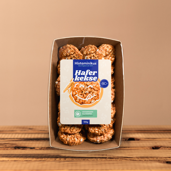 Kartonschale mit „Haferkekse“ (100 g), Etikett frontal mit BIO-Siegel; auf Holzoberfläche vor beigem Hintergrund.
