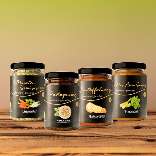 Vier histaminarme, glutenfreie Gewürze von Histaminikus in Gläsern: 5 Minuten Gemüsesuppe, Pastagewürz, Kartoffelwürze und mildes Asia Gewürz, arrangiert auf einem Holztisch vor warmem Farbverlauf-Hintergrund.