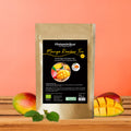Standbeutel mit der Aufschrift „Histaminikus Mango Rooibos Tee – fruchtiger Rooibos-Tee, histaminarm, glutenfrei, BIO“. Auf dem Etikett sind eine aufgeschnittene Mango, Mangostücke und eine Tasse Tee abgebildet. Der Beutel steht auf einer Holzoberfläche vor einem orangefarbenen Hintergrund, links und rechts liegen ganze und aufgeschnittene Mangos sowie grüne Blätter.
