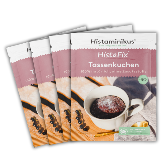 Produktbild mit vier leicht versetzt angeordneten Packungen HistaFix Tassenkuchen Bio von Histaminikus vor schwarzem Hintergrund. Die vordere Packung zeigt einen fertigen Tassenkuchen in einer weißen Tasse sowie die Hinweise „100 % natürlich, ohne Zusatzstoffe“, „Bio“ und „histaminarm, glutenfrei, laborgeprüft“.