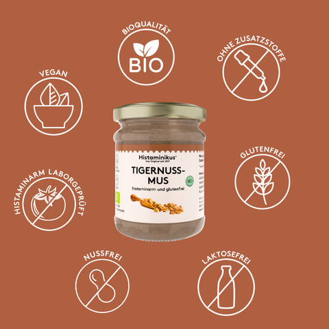 Glas Histaminikus Tigernussmus vor braunem Hintergrund, umgeben von sechs weißen Icons mit Produkteigenschaften. Oben links steht „VEGAN“ mit Pflanzensymbol, oben mittig „BIOQUALITÄT“ mit Bio-Blatt-Symbol, oben rechts „OHNE ZUSATZSTOFFE“ mit durchgestrichener Pipette. Links mittig steht „HISTAMINARM LABORGEPRÜFT“ mit durchgestrichener Tomate, rechts mittig „GLUTENFREI“ mit durchgestrichener Ähre. Unten links steht „NUSSFREI“ mit durchgestrichener Erdnuss, unten rechts „LAKTOSEFREI“ 