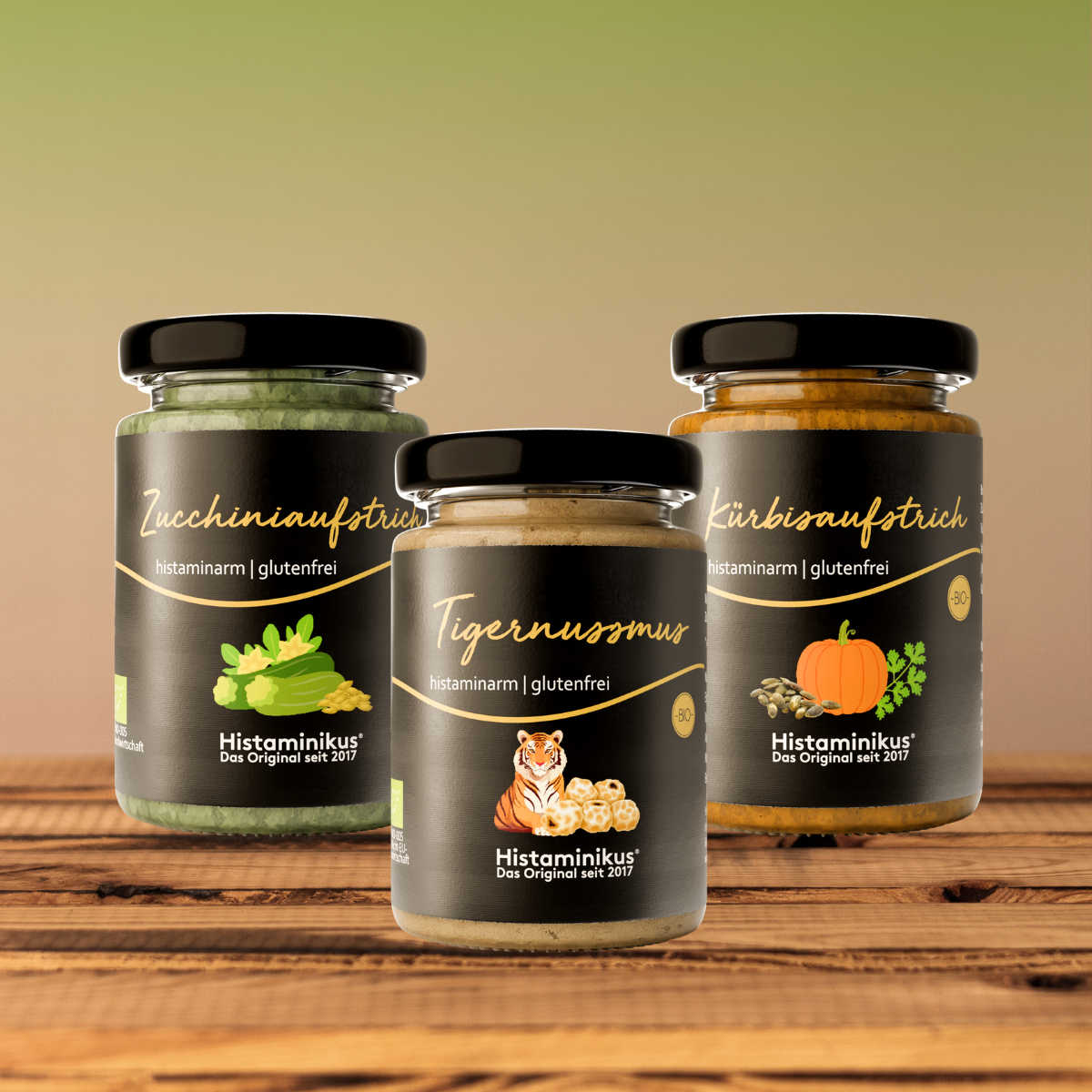 Drei histaminarme, glutenfreie Aufstriche von Histaminikus in Gläsern: Zucchiniaufstrich, Tigernussmus und Kürbisaufstrich, arrangiert auf einem Holztisch vor warmem Farbverlauf-Hintergrund.