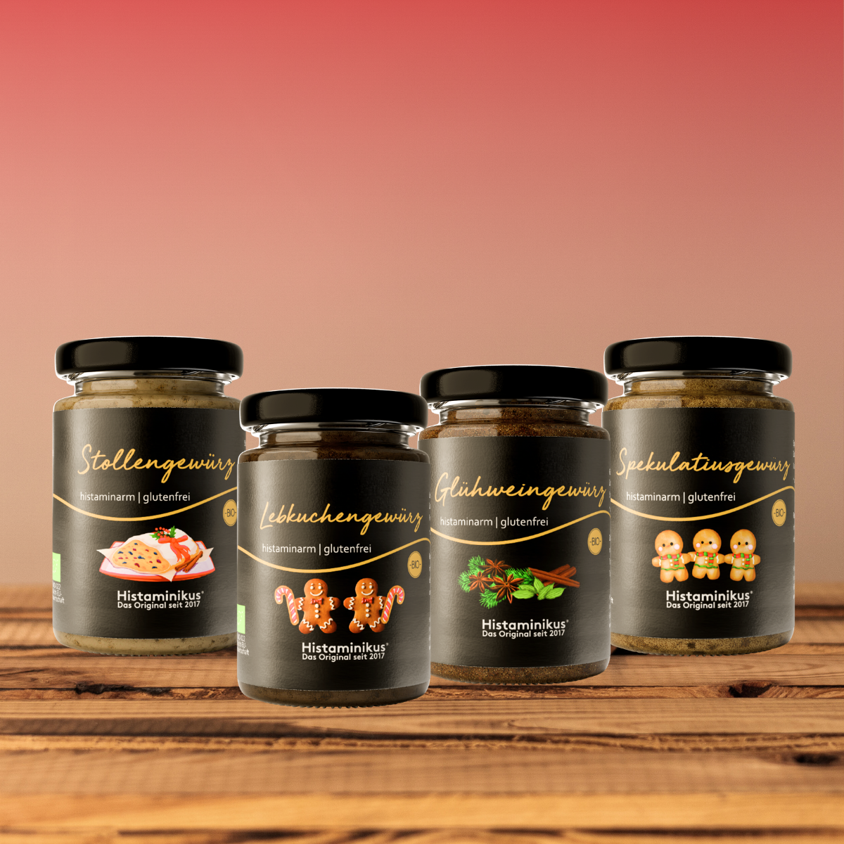 Vier histaminarme, glutenfreie Gewürzmischungen von Histaminikus in Glasgläsern: Stollengewürz, Lebkuchengewürz, Glühweingewürz und Spekulatiusgewürz, arrangiert auf einem Holztisch vor warmem Farbverlauf-Hintergrund.