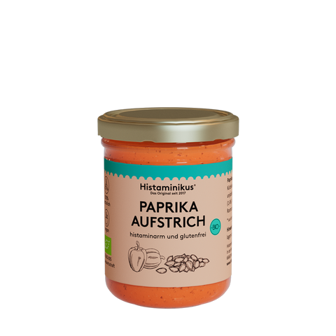 Glas mit orangem Inhalt und goldenem Deckel. Etikett mit der Aufschrift: Paprikaaufstrich. Der Inhalt wird als histaminarm und glutenfrei bezeichnet. Außerdem sind auf dem Etikett zwei Paprika und Kürbiskerne zu sehen. Das Bio-Siegel ist rechts in einem kräftigen Türkis aufgedruckt.
