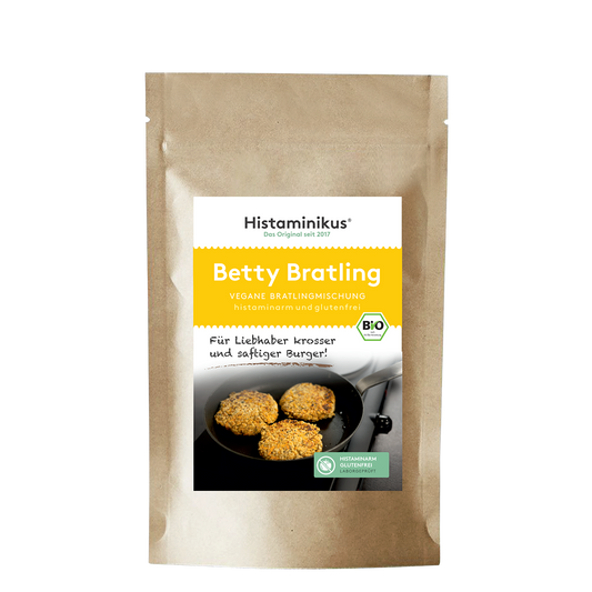 Braune Standbodenverpackung mit Etikett des Produkts „Betty Bratling“. Oben auf dem Etikett der Schriftzug „Histaminikus, Das Original seit 2017“. Darunter gelbes Feld mit Produktname „Betty Bratling“ und Hinweis „vegane Bratlingmischung, histaminarm und glutenfrei“. Im unteren Bereich des Etiketts ein Foto von drei goldbraunen Bratlingen in einer schwarzen Pfanne. BIO-Siegel und Symbol für histaminarm und glutenfrei sichtbar.