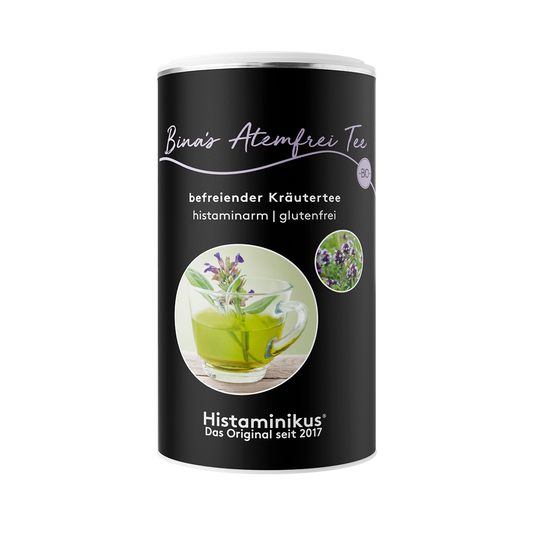 Freigestellter Packshot der runden Dose „Bina’s Atemfrei Tee“ vor weißem Hintergrund. Schwarzes Etikett mit Text „befreiender Kräutertee – histaminarm | glutenfrei“, großes Foto einer Glas-Tasse mit grünem Kräutertee und Kräutern, daneben kleine runde Detailaufnahme blühender Kräuter.