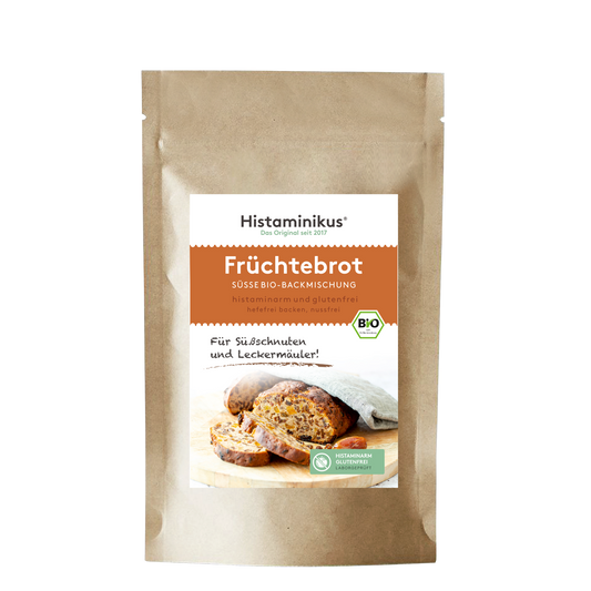 Braune Papierverpackung mit weißem Etikett. Produktname „Früchtebrot“ in orangener Schrift, darunter „süße Bio-Backmischung, histaminarm und glutenfrei“. Foto eines angeschnittenen Früchtebrots auf Holzbrett, mit Bio-Siegel und Slogan „Für Süßschnuten und Leckermäuler!“