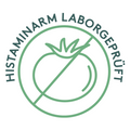 Grafik eines kreisförmigen Siegels mit einer stilisierten durchgestrichenen Tomate in der Mitte. Der umlaufende Schriftzug lautet „Histaminarm laborgeprüft“. Die Gestaltung ist in einem dezenten Grünton gehalten.