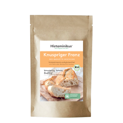 Produktabbildung der braunen Kraftpapierverpackung mit Etikett „Knuspriger Franz – Bio-Baguette-Mischung“. Untertitel: „histaminarm und glutenfrei – mit Hefe oder Backpulver backen“. Im unteren Bereich ein Foto von frisch gebackenem Baguette auf einem Holzbrett, mit dem handschriftlichen Zusatz „knusprig, kross, fluffig!“. Daneben grüne Siegel für „histaminarm glutenfrei“ und Bio-Qualität.