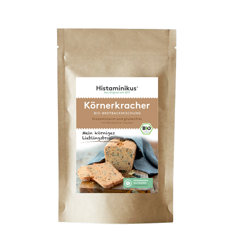 Beige Papiertüte mit Etikett. Produktname „Körnerkracher“ auf braunem Hintergrund. Darunter ein Foto eines angeschnittenen Körnerbrots mit Brotscheiben. Mit Bio-Siegel und grünem „Histaminarm – Glutenfrei – Laborgeprüft“-Label.