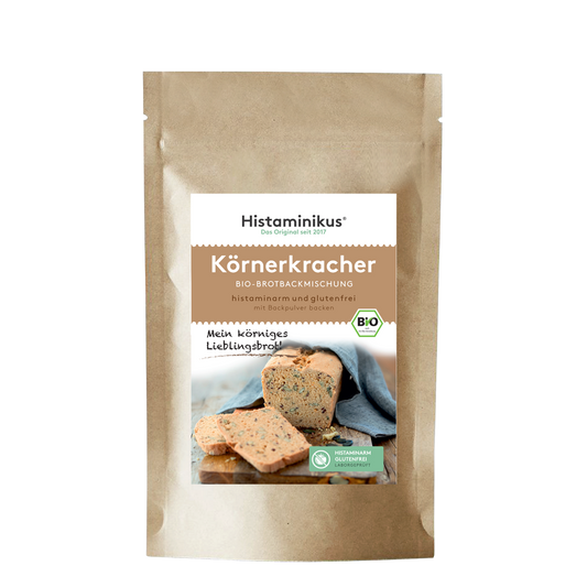 Beige Papiertüte mit Etikett. Produktname „Körnerkracher“ auf braunem Hintergrund. Darunter ein Foto eines angeschnittenen Körnerbrots mit Brotscheiben. Mit Bio-Siegel und grünem „Histaminarm – Glutenfrei – Laborgeprüft“-Label.