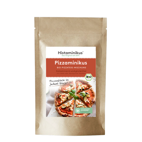 Brauner Standbodenbeutel mit zentralem, weiß-rot gestaltetem Etikett von Histaminikus; Produktname „Pizzaminikus – Bio-Pizzateig-Mischung“. Unterzeile „histaminarm und glutenfrei, mit Hefe oder Backpulver backen“. Rechts am Etikett ein grünes BIO-Siegel. Darunter Produktfoto: runde Pizza, in Stücke geschnitten, mit weißem Belag und Basilikum; daneben handschriftlicher Spruch „Pizzaglück in jedem Stück!“. Unten rechts ein grünes Siegel „Histaminarm – Glutenfrei – Laborgeprüft“.