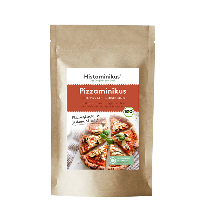 Brauner Standbodenbeutel mit zentralem, weiß-rot gestaltetem Etikett von Histaminikus; Produktname „Pizzaminikus – Bio-Pizzateig-Mischung“. Unterzeile „histaminarm und glutenfrei, mit Hefe oder Backpulver backen“. Rechts am Etikett ein grünes BIO-Siegel. Darunter Produktfoto: runde Pizza, in Stücke geschnitten, mit weißem Belag und Basilikum; daneben handschriftlicher Spruch „Pizzaglück in jedem Stück!“. Unten rechts ein grünes Siegel „Histaminarm – Glutenfrei – Laborgeprüft“.