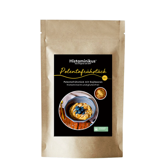 Standbeutel aus braunem Kraftpapier mit schwarzem Etikett von Histaminikus. Auf dem Etikett steht „Polentafrühstück“ sowie „Polentafrühstück mit Gojibeeren, histaminarm und glutenfrei“. Abgebildet ist eine Schale mit cremigem Polenta-Frühstück, garniert mit Heidelbeeren. Oben rechts befindet sich ein rundes Detailbild der Mischung, daneben ein gelbes BIO-Siegel. Unten rechts ist ein grünes Siegel mit dem Hinweis auf histaminarm und glutenfrei.
