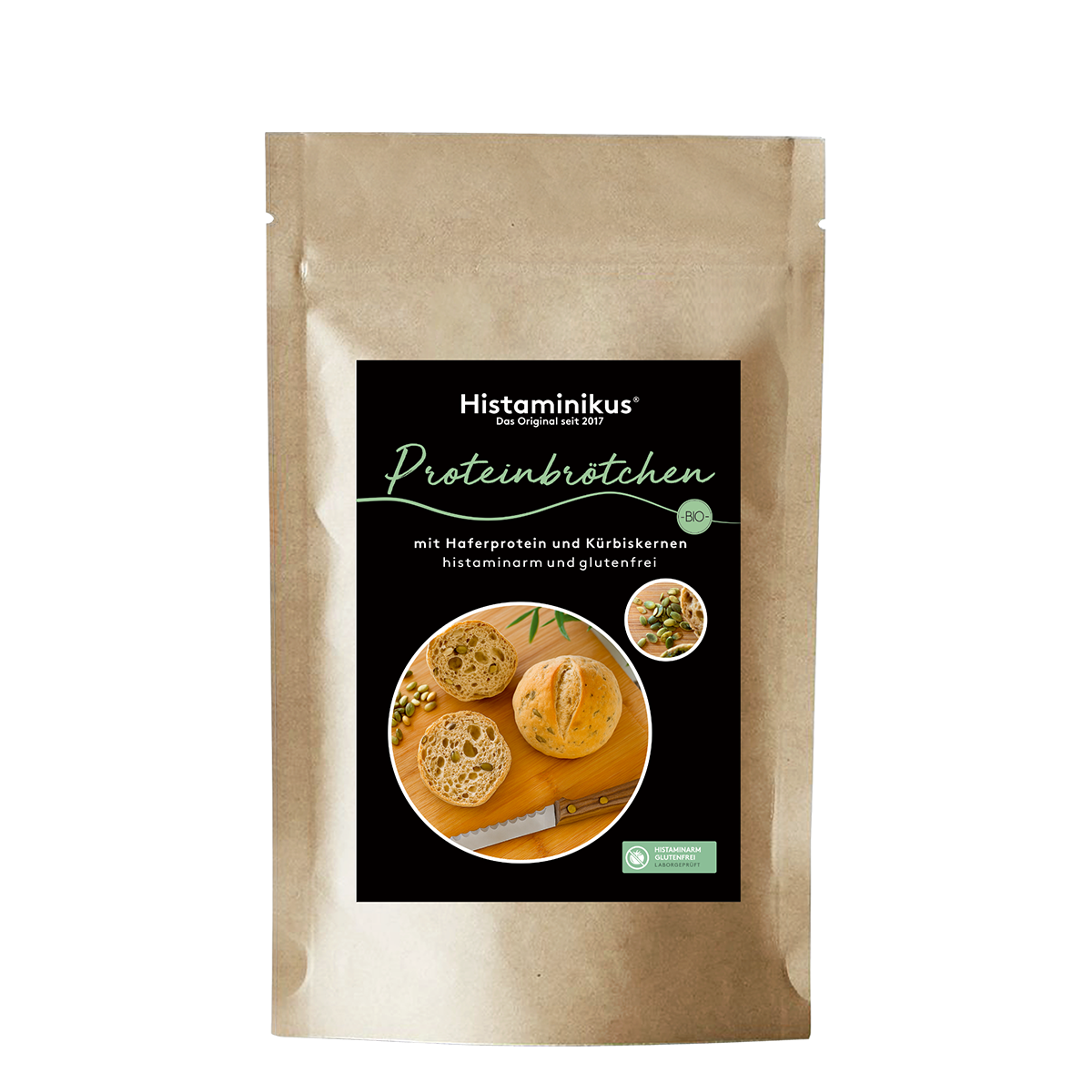 Vorderansicht einer braunen, stehenden Papiertüte mit Produktetikett „Histaminikus Proteinbrötchen“. Auf dem Etikett sind zwei runde, aufgeschnittene Brötchen mit sichtbaren Kürbiskernen sowie ein Brotmesser auf einem Holzbrett abgebildet. Die Beschriftung auf dem Etikett lautet: „mit Haferprotein und Kürbiskernen, histaminarm und glutenfrei“. Rechts oben auf dem Etikett ist ein kleines rundes Foto mit Kürbiskernen und Teigstücken zu sehen.