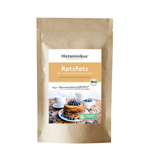 Produktfoto der „RatzFatz“ Bio-Pfannkuchenmischung von Histaminikus. Auf der braunen Standbodenverpackung befindet sich ein Etikett mit Produktnamen, Beschreibung („histaminarm und glutenfrei“) sowie einem Bild von gestapelten Pfannkuchen mit Heidelbeeren. Unten das grüne Siegel „histaminarm – glutenfrei – laborgeprüft“ und das EU-Bio-Logo.