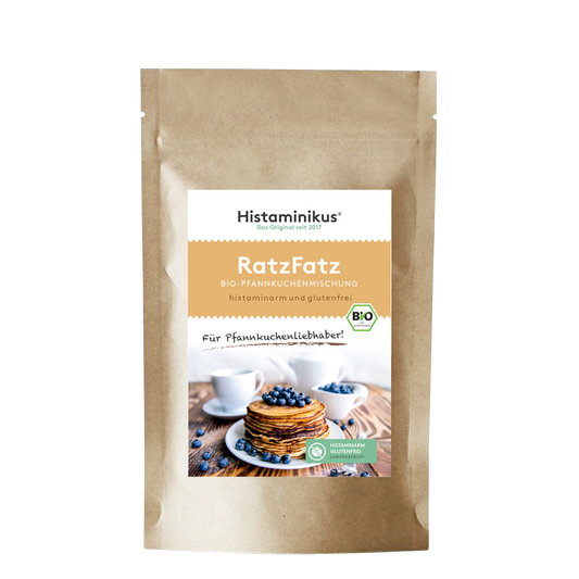 Produktfoto der „RatzFatz“ Bio-Pfannkuchenmischung von Histaminikus. Auf der braunen Standbodenverpackung befindet sich ein Etikett mit Produktnamen, Beschreibung („histaminarm und glutenfrei“) sowie einem Bild von gestapelten Pfannkuchen mit Heidelbeeren. Unten das grüne Siegel „histaminarm – glutenfrei – laborgeprüft“ und das EU-Bio-Logo.