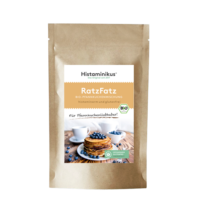 Produktfoto der „RatzFatz“ Bio-Pfannkuchenmischung von Histaminikus. Auf der braunen Standbodenverpackung befindet sich ein Etikett mit Produktnamen, Beschreibung („histaminarm und glutenfrei“) sowie einem Bild von gestapelten Pfannkuchen mit Heidelbeeren. Unten das grüne Siegel „histaminarm – glutenfrei – laborgeprüft“ und das EU-Bio-Logo.