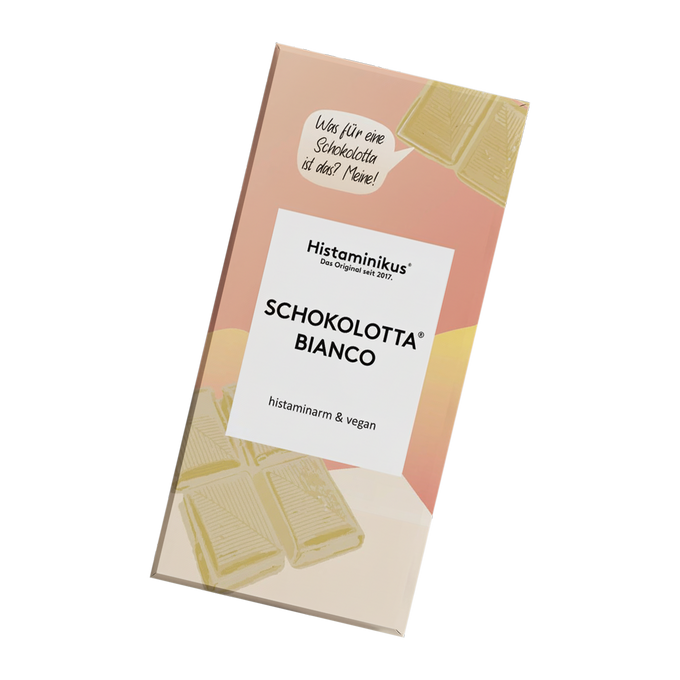 Schräg dargestellte Verpackung der veganen, histaminarmen Schokolade „Schokolotta Bianco“ von Histaminikus mit weißem Etikett, handschriftlicher Sprechblase, weißen Schokoladenstücken.
