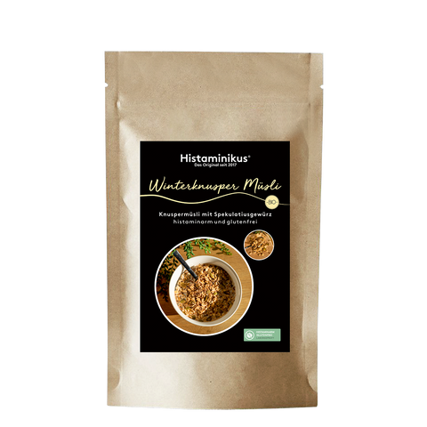 Stehende Papierverpackung „Winterknusper Müsli“ von Histaminikus  mit schwarzem Etikett, hellgelber Schrift, Abbildung einer Müslischale mit Knuspermüsli sowie Bio-Siegel und Produkthinweisen.